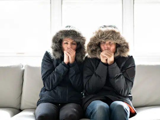 couple sitting on couch in winter jackets because heater in Colorado Springs is broken
