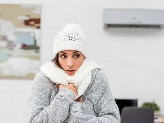 woman wearing winter coat, scarf and hat because no heat at home