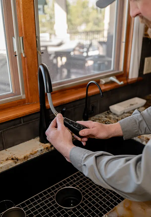 Technician adjusting kitchen sink fixture in residential home in Colorado Springs, CO.